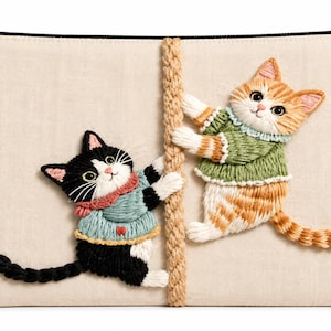 May include: A rectangular beige fabric pouch with a black zip closure. The front features an embroidered design of a black and white cat in a blue jumper and an orange tabby cat in a green jumper, both climbing a vertical tan rope.
