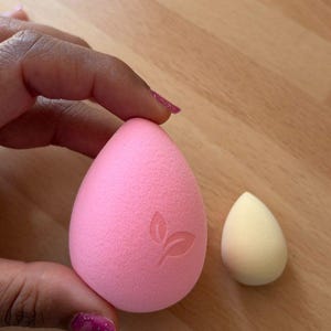 May include: Two makeup sponges. One is a large, pink, teardrop-shaped sponge with a leaf design. The other is a smaller, yellow, teardrop-shaped sponge. Both are made of a soft, porous material.