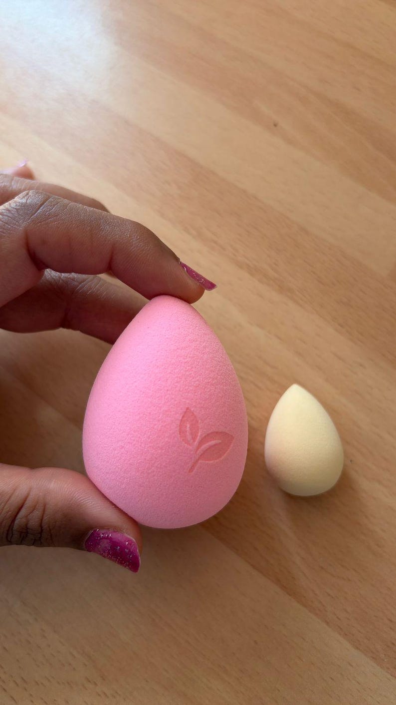 May include: Two makeup sponges. One is a large, pink, teardrop-shaped sponge with a leaf design. The other is a smaller, yellow, teardrop-shaped sponge. Both are made of a soft, porous material.
