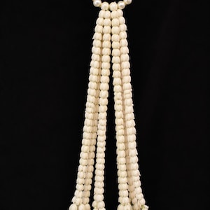 May include: A decorative garland featuring a circular loop of white faux pearls at the top, from which hang four long, vertical strands of small, cream-colored, bud-like floral elements, each ending in a cluster of tightly packed flower buds.