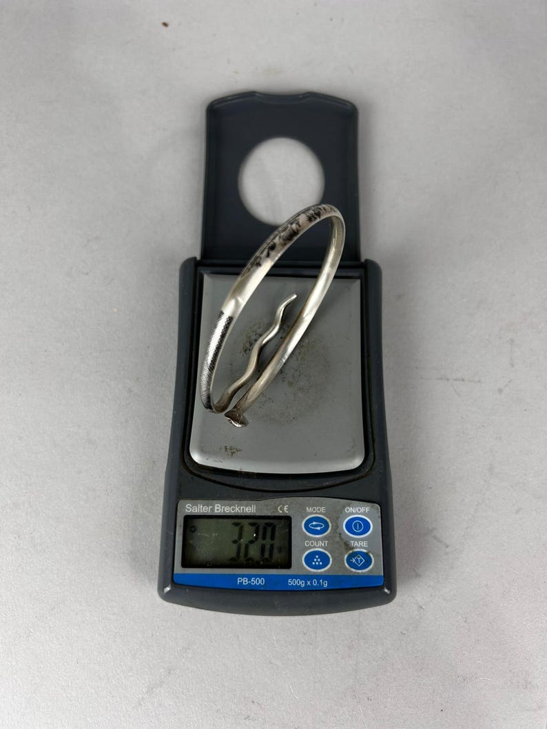 May include: A silver bracelet with a decorative design is placed on a digital scale. The scale displays a weight of 32.0. The scale is a Salter Brecknell PB-500 model.