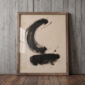 Puede incluir: Una pieza de arte mural enmarcada que presenta una gran pincelada negra en forma de media luna sobre una pincelada negra horizontal en un fondo de color crema. La obra está encerrada en un marco de madera marrón claro con veta visible.