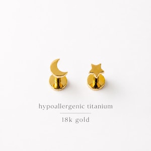 May include: Two gold-colored, hypoallergenic titanium earrings. One is a crescent moon shape, and the other is a star shape. The earrings are 18k gold. The text in the image reads: hypoallergenic titanium, 18k gold.