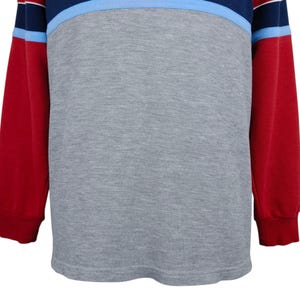 Puede incluir: Una camiseta de manga larga con un dise&ntilde;o de bloques de color. La camiseta presenta un cuerpo gris, mangas rojas y una pechera a rayas azul marino y celeste. Los pu&ntilde;os y el cuello son acanalados.