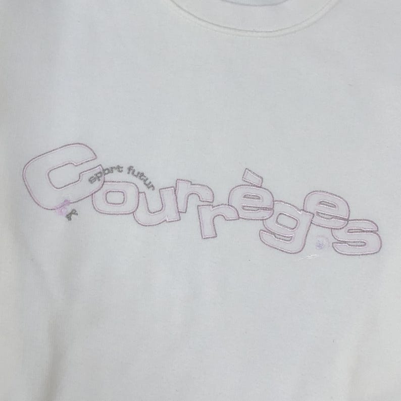 以下が含まれることがあります： 薄いピンク色の糸で刺繍されたCourr&egrave;gesという文字が特徴の白いスウェットシャツ。文字の縁は細いダークカラーで囲まれています。メインの文字の上には曲線状のフォントでsport futurという小さな単語が添えられ、小さなリボンの装飾が施されています。