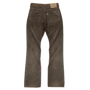 May include: A pair of brown corduroy pants shown from the back, featuring two rear pockets, a waistband with belt loops, and a tan leather-colored brand patch on the right side of the waist. The fabric has a visible vertical ribbed texture.