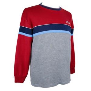 Puede incluir: Una sudadera de manga larga roja, gris y azul. La parte superior es roja, con una franja azul marino y celeste en el pecho. La mitad inferior es gris. El logotipo de Fila est&aacute; en la parte superior derecha del pecho.