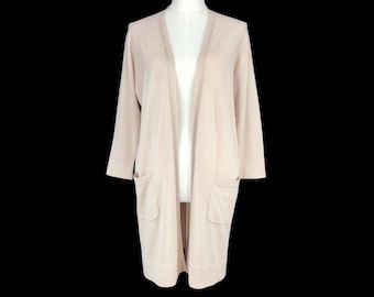 May include: A long, open-front cardigan in a light beige color. The cardigan features long sleeves that end just below the elbow and two front pockets. The garment is displayed on a mannequin against a black background.