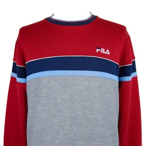 Puede incluir: Una sudadera Fila roja, gris y azul. La parte superior es roja, con una franja azul marino y azul claro en el pecho. La mitad inferior es gris. El logotipo de Fila est&aacute; bordado en la parte superior derecha del pecho.