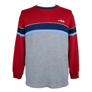 Puede incluir: Una sudadera de manga larga roja, azul marino, azul claro y gris. La parte superior es roja, con una franja azul marino y azul claro en el pecho. La mitad inferior es gris. El logotipo de Fila est&aacute; en la parte superior del pecho.
