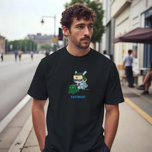 May include: A black short-sleeve t-shirt featuring a graphic of a light blue rabbit wearing a green ushanka hat with a red star and sunglasses, sitting next to a small green robot. The text FASTBOOT is printed in blue below the graphic.