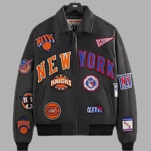 Puede incluir: Chaqueta de cuero negra con m&uacute;ltiples parches con balones de baloncesto y las palabras "NEW YORK" en naranja y azul. La chaqueta tiene un estilo bomber, con cuello y cierre de cremallera.