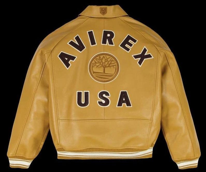 May include: Mustard yellow leather jacket with the word "AVIREX" arched across the back in brown block letters. Below the brand name is a circular emblem and the word "USA". The jacket has a collared neckline and ribbed cuffs and hem.