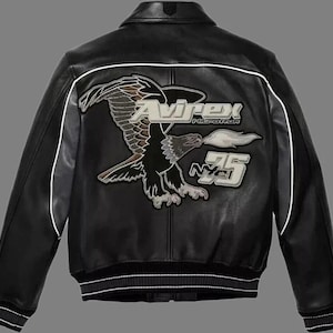 May include: Black leather jacket with white trim and a ribbed hem. The back features a large embroidered eagle graphic with the brand name "Avirex" and the number "75".