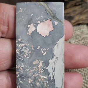 Può includere: Una pietra rettangolare con un motivo unico. La pietra presenta una miscela di colori grigio, rosa e crema. Il design include macchie rosa e crema su uno sfondo grigio, creando un aspetto naturale e strutturato.