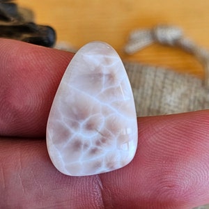 Puede incluir: Una piedra de ágata blanca y gris con un patrón de remolino. La piedra es lisa y pulida.