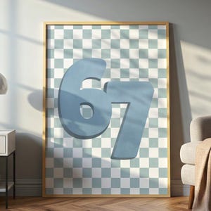 May include: A framed print displaying the number '67' in light blue. The numbers are prominent against a backdrop of a light blue and white checkered pattern. The frame is a warm gold colour.