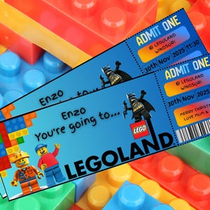May include: Two blue Legoland Windsor tickets with Batman and Lego figures. The tickets read "Enzo, You're going to..." and "Admit One" with the date November 30, 2025. The background is colorful Lego blocks.