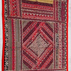 May include: A rectangular, ornate textile in shades of red, burgundy, and gold. The piece features intricate patterns, including geometric shapes and floral motifs, with a vibrant red border. This decorative textile is suitable for wall hangings or as a decorative throw.