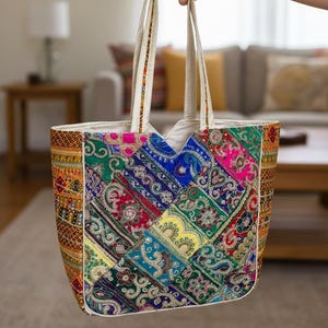 Puede incluir: Un bolso tote colorido con un diseño de patchwork. El bolso presenta una variedad de colores vibrantes, incluyendo rosa, azul, verde y amarillo. Las asas son de color crema y el bolso es sostenido por una mano.