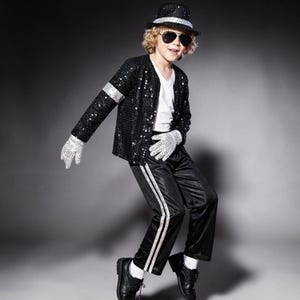 Puede incluir: Una chaqueta negra de lentejuelas con brazalete plateado, una camiseta blanca de cuello en V, pantalones negros con doble raya lateral plateada, un sombrero fedora negro de lentejuelas con banda plateada, gafas de sol, guantes blancos de lentejuelas y zapatos de vestir negros.