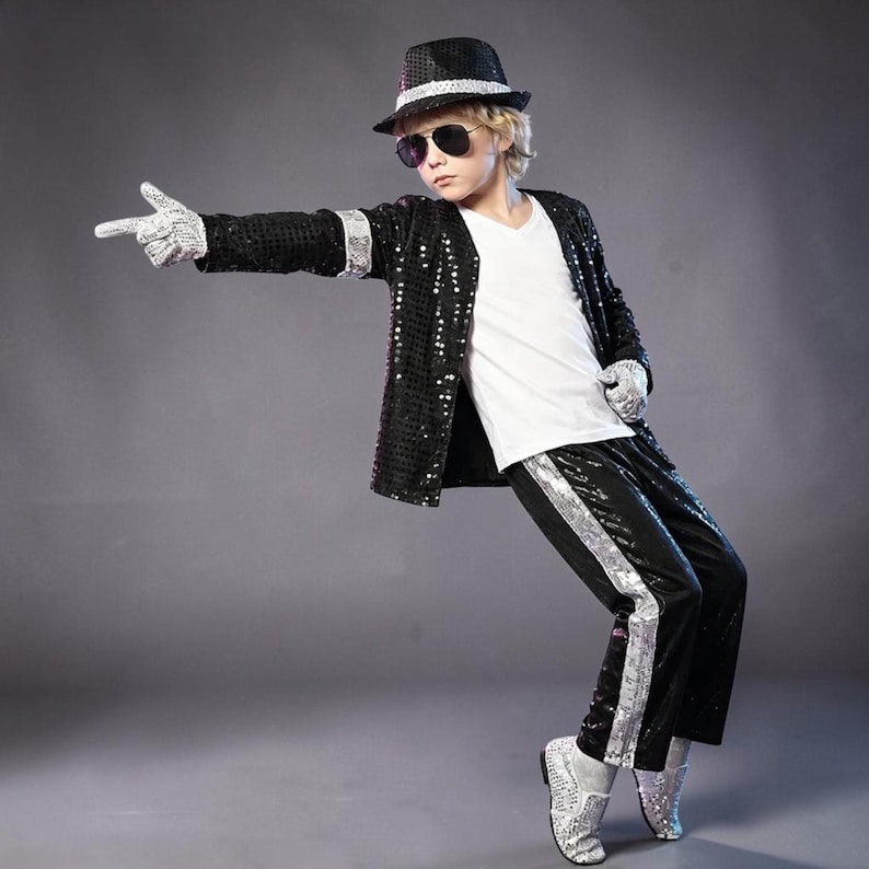 Puede incluir: Una chaqueta negra de lentejuelas con ribete plateado, pantalones negros de lentejuelas con una franja lateral plateada, una camiseta blanca con cuello en V, un sombrero fedora negro con banda plateada, guantes de lentejuelas y zapatos plateados.