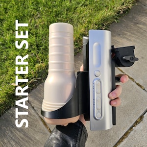 May include: A starter set featuring a cream-colored, ribbed cylindrical object held in a black bracket, paired with a silver device with buttons. The text "STARTER SET" is vertically displayed in white.