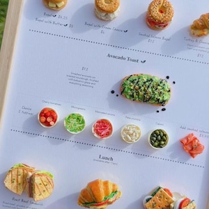 Peut inclure: Un menu avec des modèles réduits de plats. Le petit-déjeuner propose des bagels avec du beurre et du fromage à la crème, et un bagel au saumon fumé. Le déjeuner propose un sandwich au rosbif, un croissant au jambon et au fromage, et un sandwich Caprese.