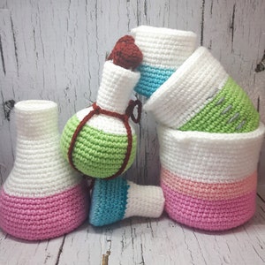 May include: A set of five crocheted bottle-shaped containers in various colors, including white, pink, green, and blue. The containers are stacked on top of each other.
