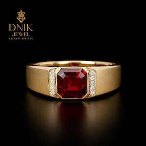 Op de afbeelding: Een gouden ring met een grote, vierkante, dieprode edelsteen in het midden. Kleine, heldere edelstenen zijn aan weerszijden van de centrale steen gezet. De ring heeft een geborstelde afwerking. De tekst "DNIK JEWEL Elegant Jewelry" staat linksboven.
