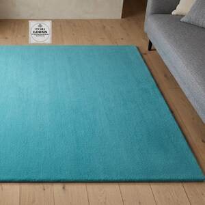 May include: A rectangular area rug in a solid, vibrant turquoise blue color with a soft, plush texture. The rug features a small white square logo in the center top edge with the text EVARA LOOMS printed in black lettering on the surface.