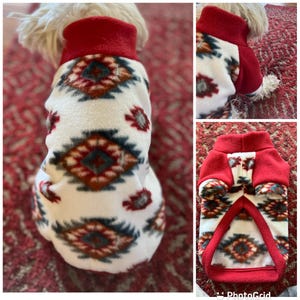 May include: White fleece dog sweater with a red collar and a geometric pattern in shades of red, brown, blue, and gray.