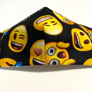 May include: Black face mask with a yellow emoji pattern. The emojis include winking, smiling, and heart-eyed faces.