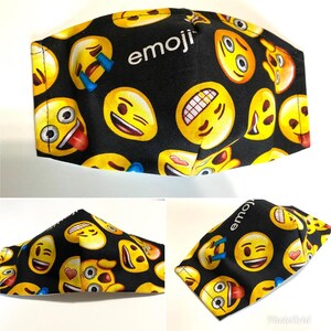 May include: Black fabric face mask with a repeating pattern of yellow emoji faces. The text "emoji" is printed in white on the mask.