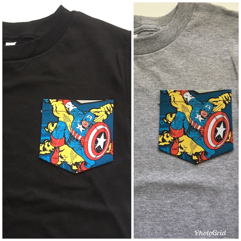 Puede incluir: Dos camisetas, una negra y otra gris, con un bolsillo que presenta una imagen de Captain America al estilo de un c&oacute;mic. La imagen muestra a Captain America con su ic&oacute;nico traje rojo, blanco y azul, sosteniendo su escudo y volando por el aire.