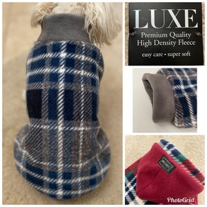 May include: A blue and gray plaid dog sweater with a gray fleece lining. The sweater has a high neck and is made of high density fleece. The tag says "LUXE Premium Quality High Density Fleece easy care - super soft".