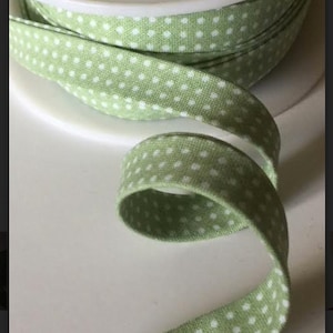 May include: A roll of green and white polka dot fabric trim. The trim is folded and rolled up on a spool.