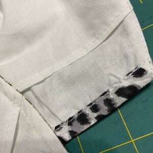 May include: Close-up of a white fabric with a black and white animal print fabric sewn to the edge. The fabric is on a green cutting mat.