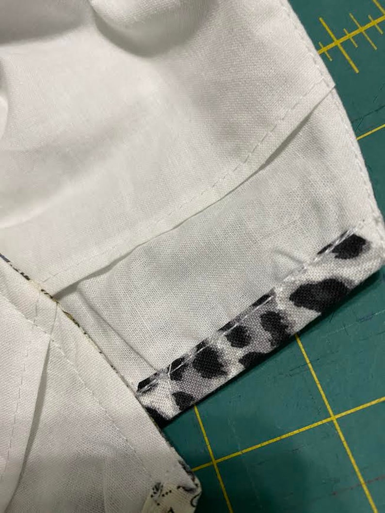 May include: Close-up of a white fabric with a black and white animal print fabric sewn to the edge. The fabric is on a green cutting mat.