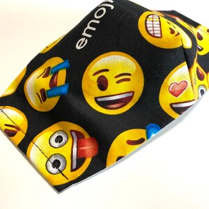 May include: Black fabric face mask with a repeating pattern of yellow emoji faces. The text "emoji" is printed in white on the top of the mask.
