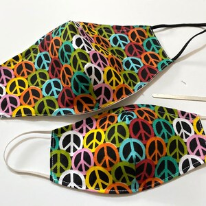 May include: Two face masks with a colorful peace sign pattern. The larger mask has black elastic ear loops and the smaller mask has white elastic ear loops.