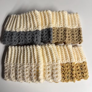 May include: Handmade crochet headbands in cream, gray, and tan. The headbands have a ribbed design with a textured bottom border. The cream-colored headbands have gray and tan accents. The headbands are made of soft yarn.