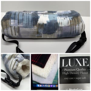 May include: A cylindrical fleece hand warmer featuring a blue, white, and gray plaid pattern with a black adjustable strap and buckle. The interior is lined with white sherpa fleece. A product tag reads LUXE Premium Quality High Density Fleece.