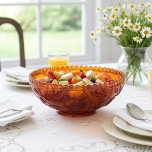Puede incluir: Un cuenco grande y redondo de cristal color ámbar con un borde festoneado y motivos florales en relieve en el exterior, lleno de una colorida ensalada de frutas con rodajas de plátano, fresas, arándanos y gajos de naranja.