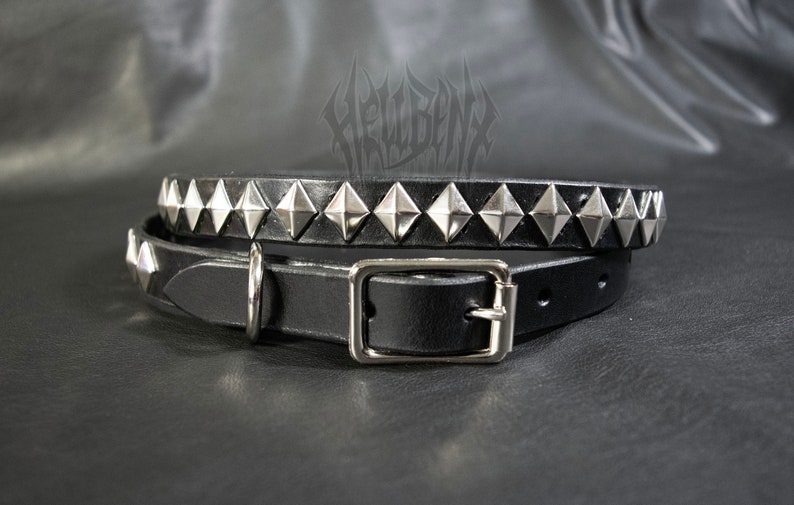 Puede incluir: Un collar de cuero negro con tachuelas de pir&aacute;mide plateadas. El collar tiene un cierre de hebilla y un anillo en D.