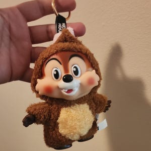 May include: A white ceramic mug with a black handle and the text "But First, Coffee" in a bold, black font. The mug is set against a blurred background, suggesting a cozy setting.
