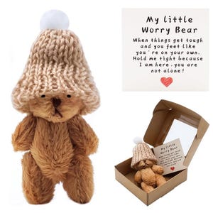 May include: A small, brown teddy bear wearing a tan knit hat with a white pom-pom. The bear is presented in a cardboard box with a small card that reads "My little Worry Bear". The card includes a message of comfort and support.