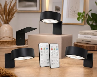 May include: Three matte black circular wall-mounted LED lamps with adjustable heads, each featuring four internal light points. Two white rectangular remote controls with various color and timer buttons are positioned in the center of the display.