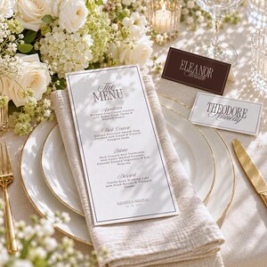 May include: A white paper menu with black text titled The Menu, featuring courses like Appetizer, First Course, Entree, and Dessert. Beside it are two white place cards with black text reading Eleanor Smith and Theodore Kennedy.