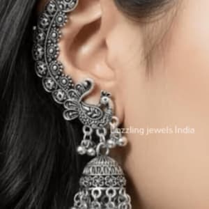 May include: An oxidized silver ear cuff featuring an intricate peacock motif with detailed feather patterns extending along the ear cartilage, accented by small dangling silver beads and a bell-shaped jhumka charm at the base of the earring.
